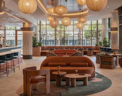 Interior view of a modern lounge area with an eye-catching bar, comfortable seating arrangements in warm, earthy tones, and large windows offering a glimpse of the outdoors.
