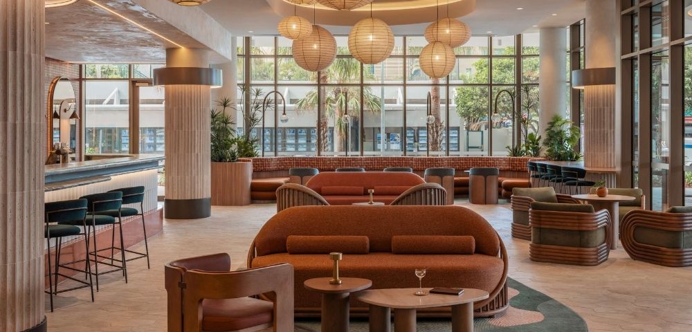 Interior view of a modern lounge area with an eye-catching bar, comfortable seating arrangements in warm, earthy tones, and large windows offering a glimpse of the outdoors.