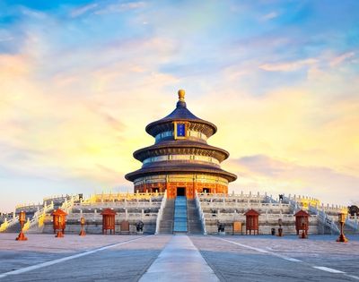 The Hall of Prayer for Good Harvests at the Temple of Heaven in Beijing, China, with its distinctive circular, multi-tiered roof, set against a vibrant sunset sky.
