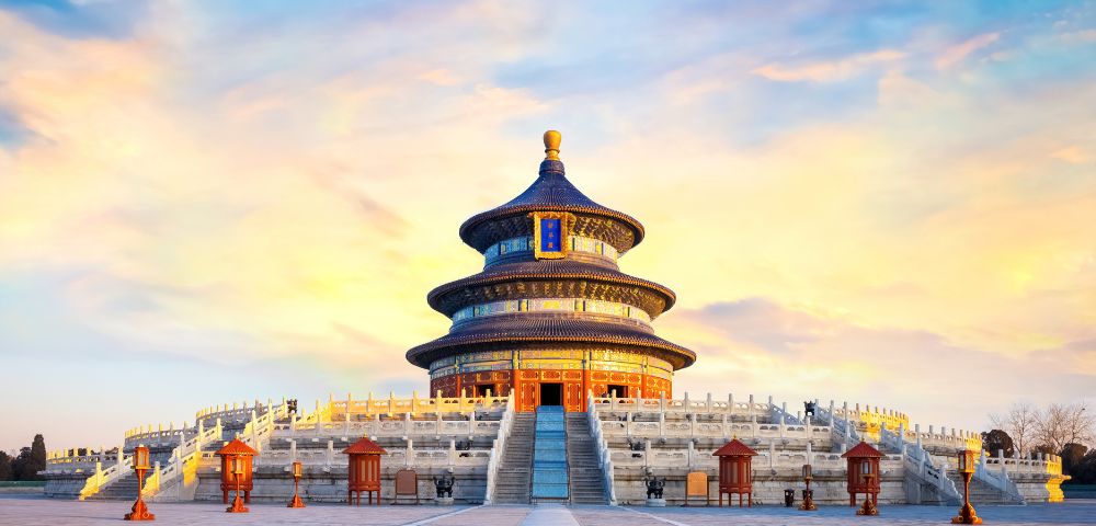 The Hall of Prayer for Good Harvests at the Temple of Heaven in Beijing, China, with its distinctive circular, multi-tiered roof, set against a vibrant sunset sky.