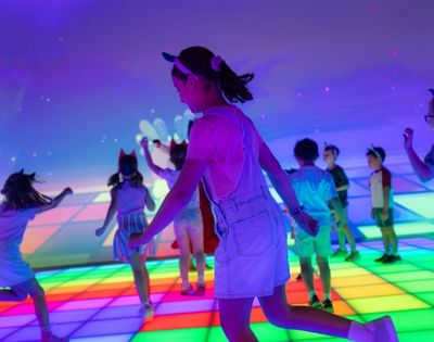 Children dance on a brightly lit, interactive floor that displays a colorful grid pattern.