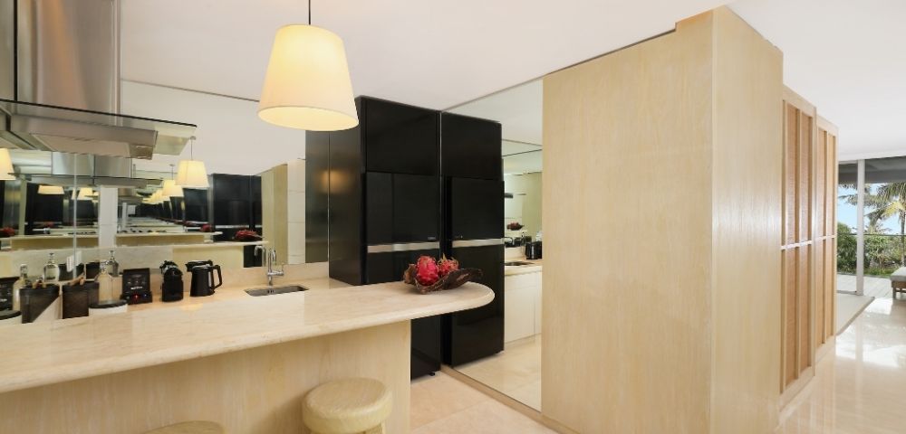 Bright minimalist kitchen with a pale wood island, cream stools, pendant lights, black cabinets, red flowers, and mirrored walls.