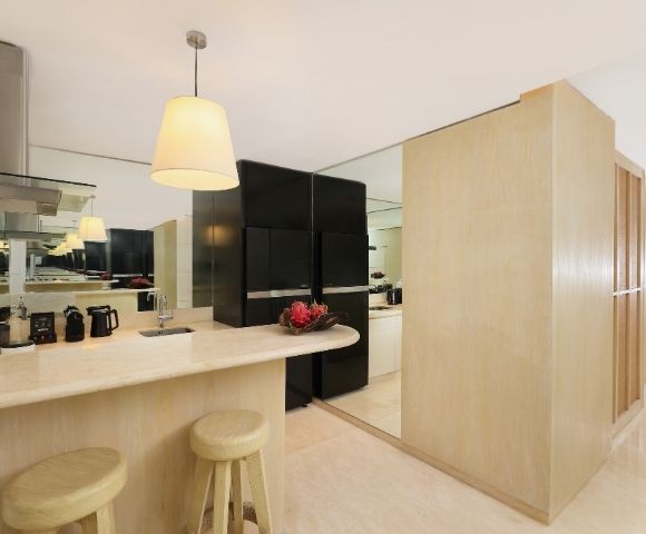 Bright minimalist kitchen with a pale wood island, cream stools, pendant lights, black cabinets, red flowers, and mirrored walls.