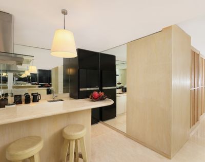 Bright minimalist kitchen with a pale wood island, cream stools, pendant lights, black cabinets, red flowers, and mirrored walls.