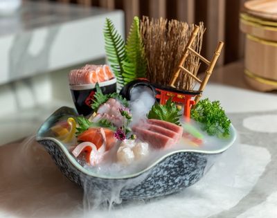 Japanese sushi boat platter with salmon, shrimp, tuna, roe, greens, and flowers, styled with bamboo, fern, and mist for a serene mood.