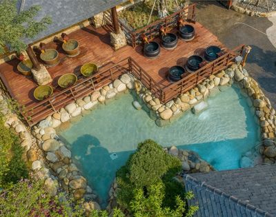 Aerial view of a natural hot spring area with stone pools and seating areas surrounded by greenery.
