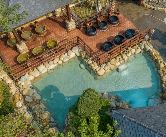 Aerial view of a natural hot spring area with stone pools and seating areas surrounded by greenery.