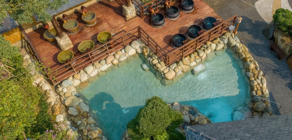 Aerial view of a natural hot spring area with stone pools and seating areas surrounded by greenery.