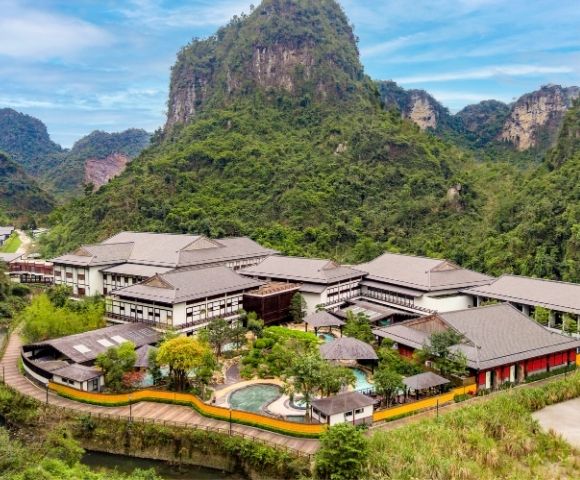 Aerial view of a modern resort surrounded by lush greenery and mountains.