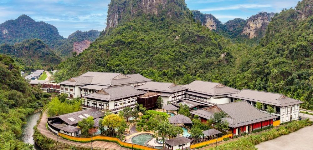 Aerial view of a modern resort surrounded by lush greenery and mountains.