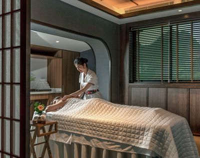 A woman giving a massage to a person lying on a treatment table in a serene spa setting.