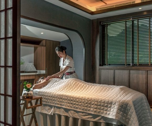 A woman giving a massage to a person lying on a treatment table in a serene spa setting.