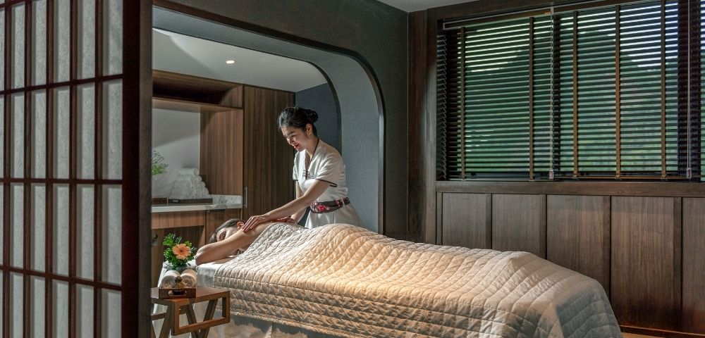 A woman giving a massage to a person lying on a treatment table in a serene spa setting.