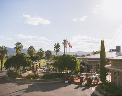 An elevated view of a resort with palm trees, an outdoor seating area with tables and chairs, flags flying, and buildings under a bright, sunny sky.