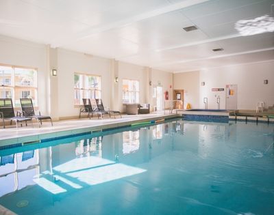Indoor swimming pool with lounge chairs and a hot tub.