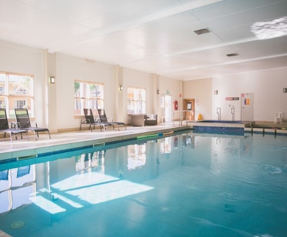 Indoor swimming pool with lounge chairs and a hot tub.