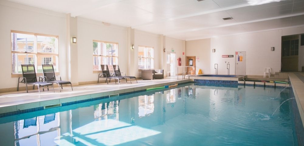 Indoor swimming pool with lounge chairs and a hot tub.