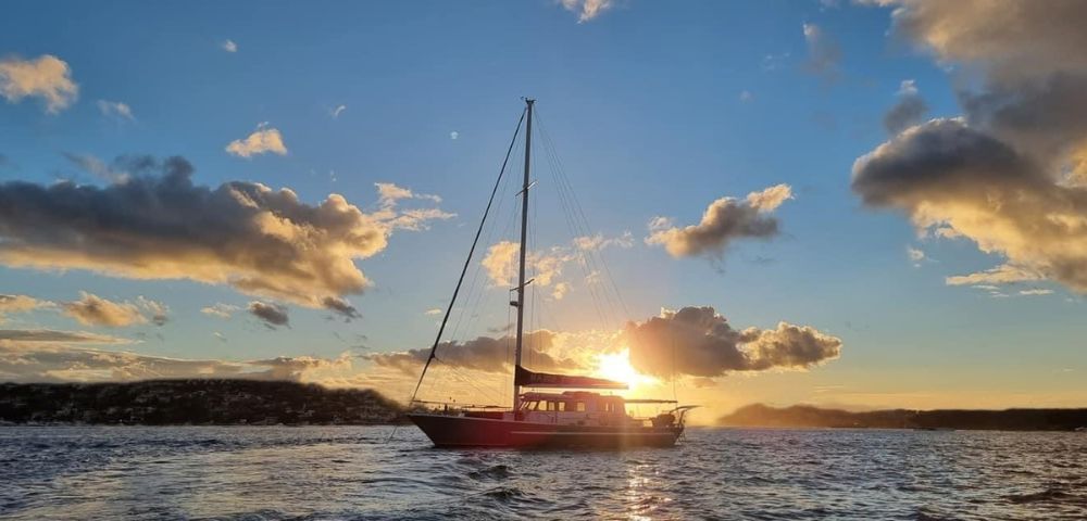 Sailboat floating on calm water at sunset with a partly cloudy sky and distant land on the horizon.