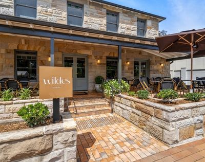 A stone building with a covered entrance and an outdoor dining area. A sign with 
