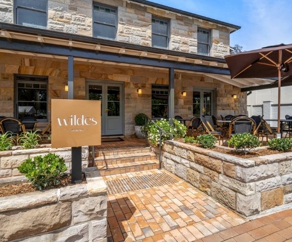 A stone building with a covered entrance and an outdoor dining area. A sign with 