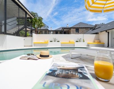 A bright, sunny day over a modern outdoor swimming pool area with yellow-cushioned lounge benches and a striped umbrella.