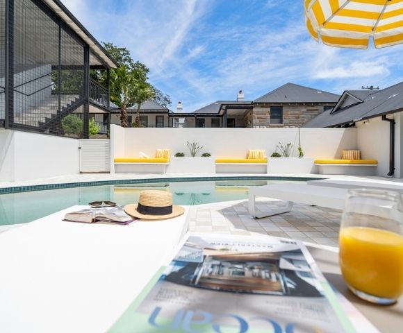 A bright, sunny day over a modern outdoor swimming pool area with yellow-cushioned lounge benches and a striped umbrella.