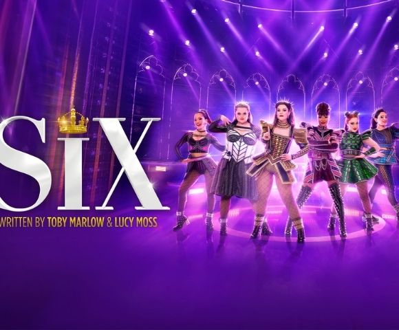 Promotional image for SIX: six women in glittering Tudor-inspired costumes perform on a purple-lit stage, with bold title text and a crown.