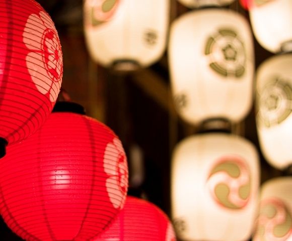 Close-up of glowing red and white paper lanterns with Japanese-style designs, creating a warm, festive atmosphere.