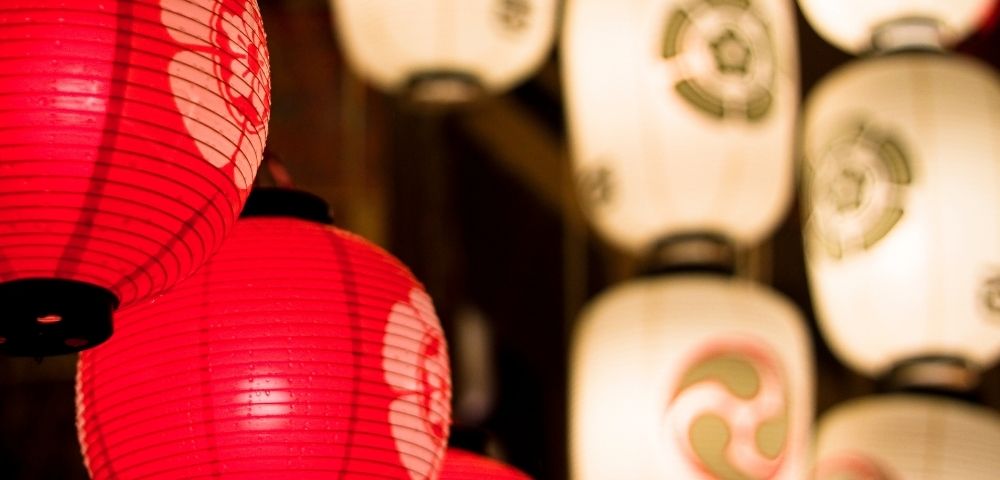 Close-up of glowing red and white paper lanterns with Japanese-style designs, creating a warm, festive atmosphere.