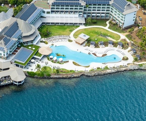 Aerial view of a resort complex with a large, freeform swimming pool and a waterfront view.