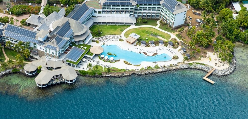 Aerial view of a resort complex with a large, freeform swimming pool and a waterfront view.
