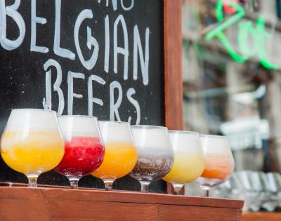 Colorful Belgian beers in tasting glasses line a bar beneath a chalkboard reading “Belgian Beers,” creating a lively, inviting pub atmosphere.