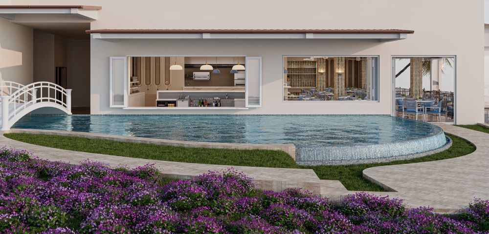 A contemporary resort scene with a crescent-shaped swimming pool in the foreground, featuring a cascading waterfall edge. Behind the pool, an open-concept bar and kitchen area is visible through large windows, complete with modern appliances and stocked shelves. To the right, a dining area with tables and chairs is set up under a covered patio, hinting at an adjacent restaurant. Lush green grass and vibrant purple flowers create a serene and inviting atmosphere around the pool.