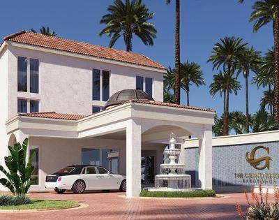 A white luxury sedan is parked at the entrance of a modern resort with palm trees in the background.