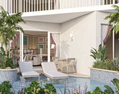 A luxurious hotel suite with a private patio featuring lounge chairs, a table with chairs, lush tropical plants, and a pool.
