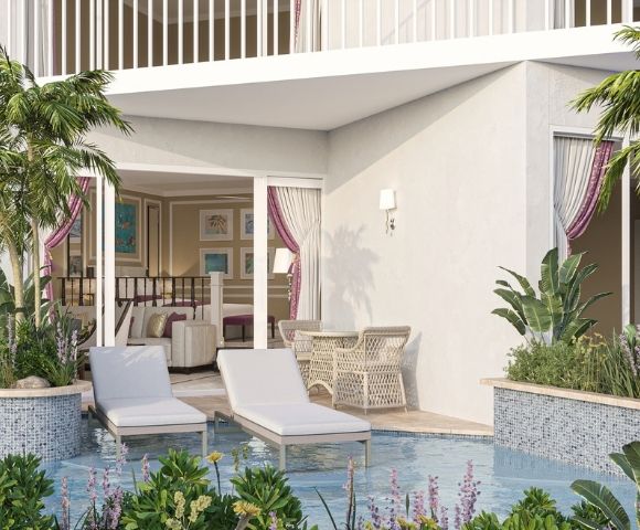 A luxurious hotel suite with a private patio featuring lounge chairs, a table with chairs, lush tropical plants, and a pool.
