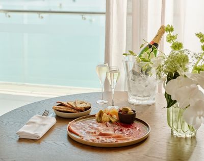 Elegant seaside brunch table with salmon platter, toast and fruit, champagne flutes, flowers, and an ice bucket, creating a serene mood.