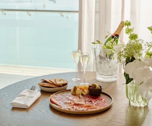 Elegant seaside brunch table with salmon platter, toast and fruit, champagne flutes, flowers, and an ice bucket, creating a serene mood.