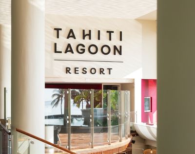 Bright Tahiti Lagoon Resort lobby with bold wall signage, glass doors, tropical palms, and ocean views creating a welcoming island atmosphere.