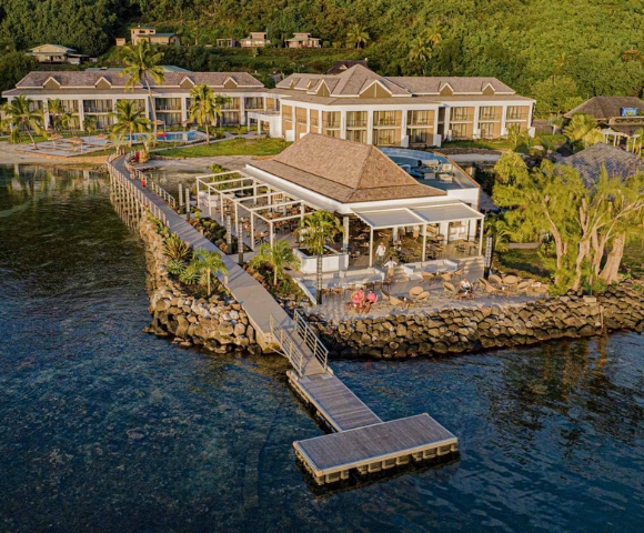 Architectural rendering of a modern waterfront home with stone retaining walls, patio, trees, and a long dock over calm blue water; serene setting.