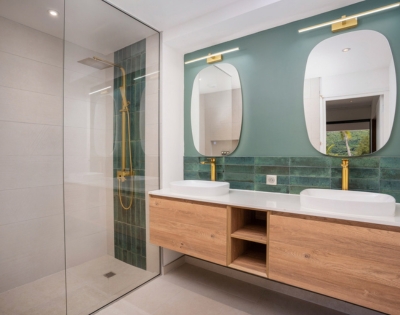 Modern bathroom vanity with two sinks, wall-mounted mirrors, teal tile backsplash, and wood cabinetry; clean geometric lines create a calm, polished atmosphere.