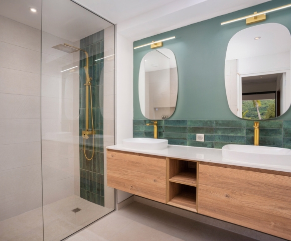 Modern bathroom vanity with two sinks, wall-mounted mirrors, teal tile backsplash, and wood cabinetry; clean geometric lines create a calm, polished atmosphere.