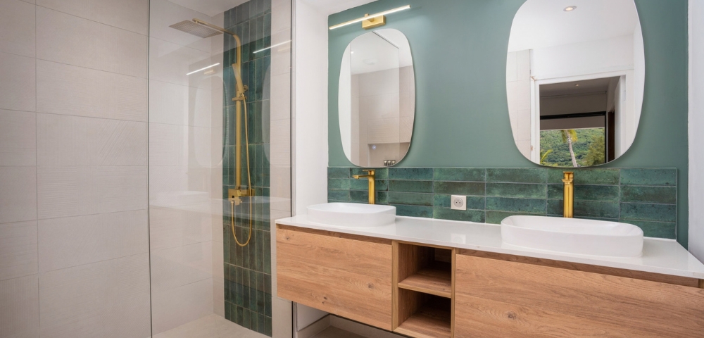 Modern bathroom vanity with two sinks, wall-mounted mirrors, teal tile backsplash, and wood cabinetry; clean geometric lines create a calm, polished atmosphere.