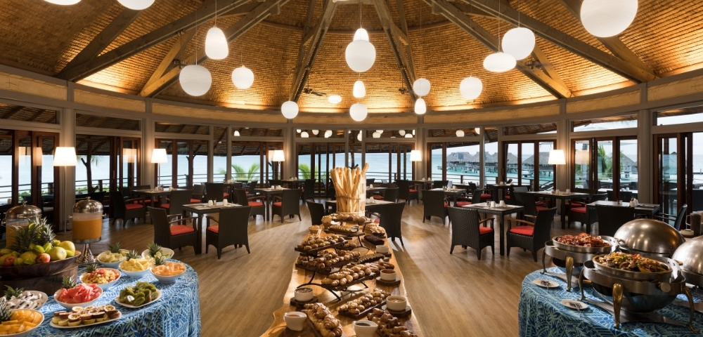 A spacious restaurant dining area filled with tables and a variety of dishes displayed on a buffet.