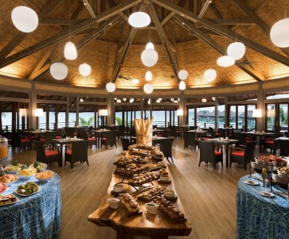 A spacious restaurant dining area filled with tables and a variety of dishes displayed on a buffet.