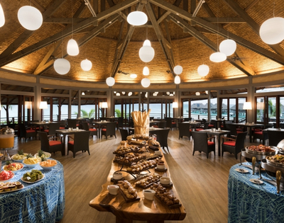 A spacious restaurant dining area filled with tables and a variety of dishes displayed on a buffet.