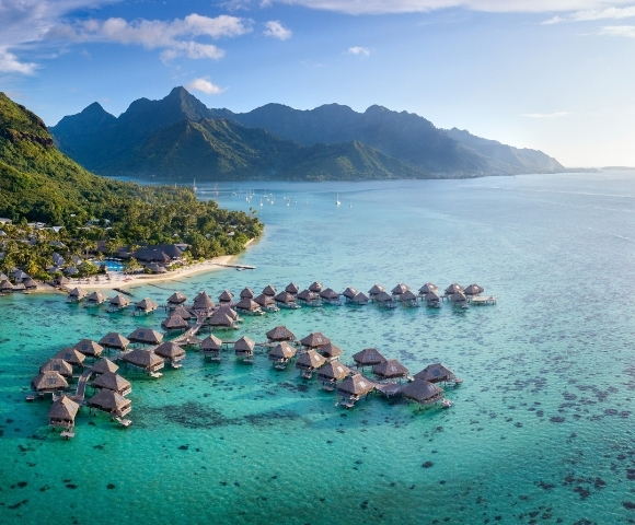 Aerial view of luxurious overwater bungalows in Bora Bora, surrounded by turquoise waters and lush greenery.