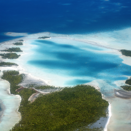 Aerial view of turquoise lagoons, white sandbars, and lush green islands surrounded by deep blue ocean.