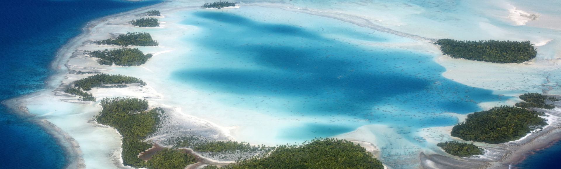 Aerial view of turquoise lagoons, white sandbars, and lush green islands surrounded by deep blue ocean.