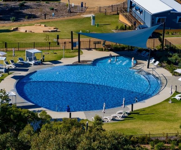An aerial view of a large, blue, multi-level swimming pool with several people playing in the shallow end and lounging chairs around the perimeter.